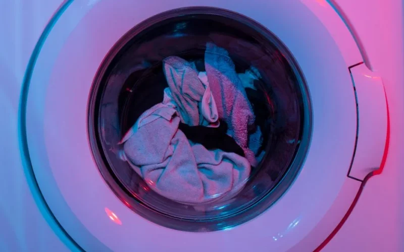 Colorful washing machine with clothes inside, lit by vivid purple and blue lights.