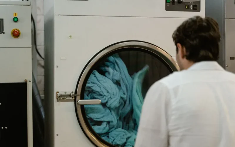 A man watches a washing machine spin in a laundromat, focusing on the process.