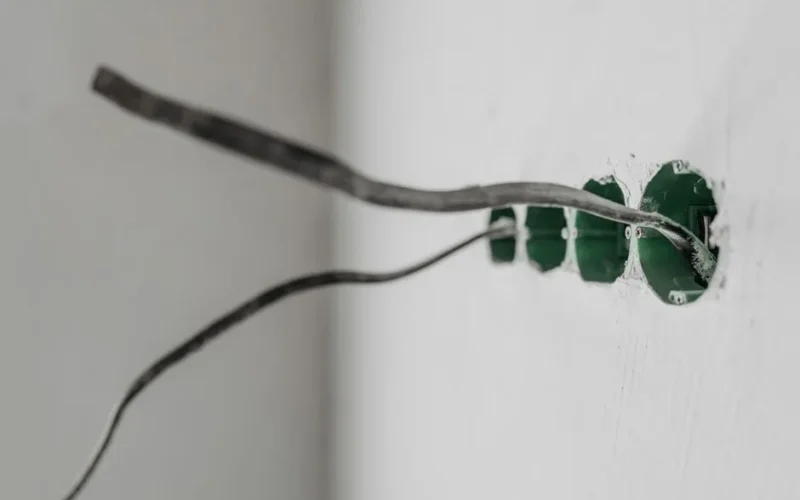Unfinished electrical outlet installation with exposed wires on a white wall.