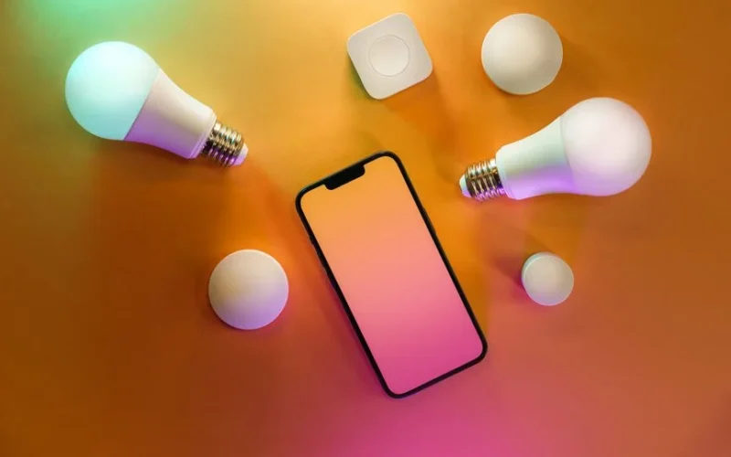 Top view of a smartphone with smart bulbs on a vibrant yellow background, depicting modern technology.