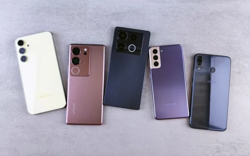 Flat lay of five modern smartphones on a gray surface, showcasing various designs.