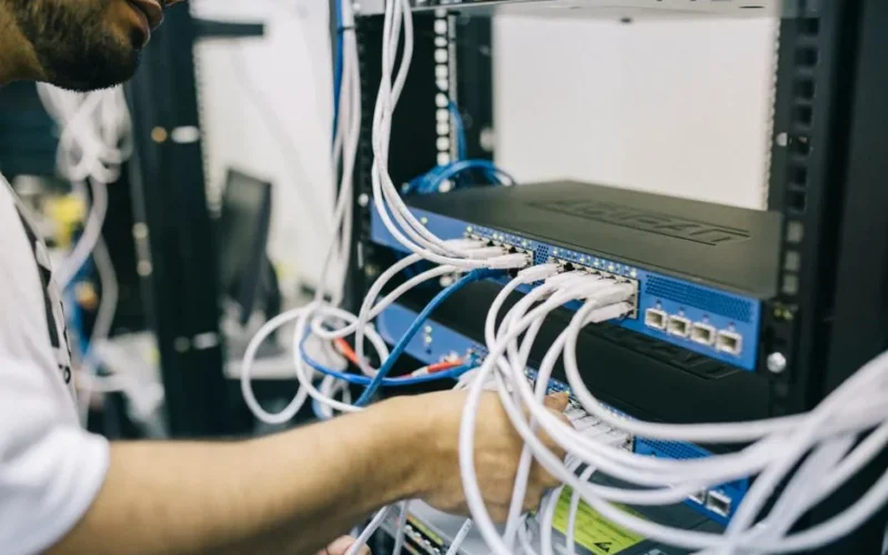 An IT professional configuring network cables in a server rack, focusing on Ethernet connections.