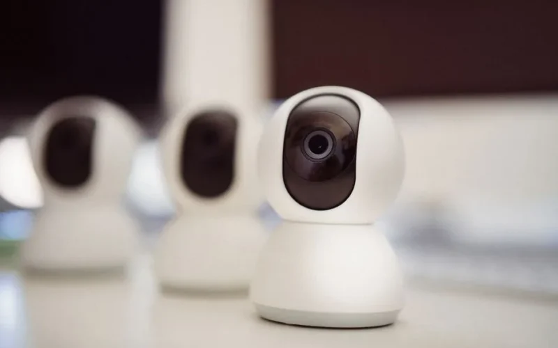 Close-up of three smart home security cameras placed on a white desk indoors.