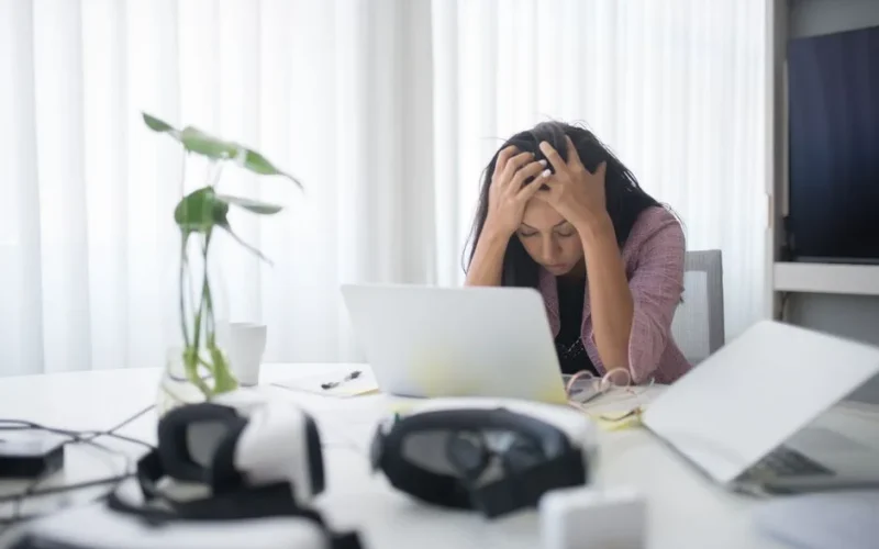 Frustrated woman sitting at desk with laptop, showing stress in a modern office environment.