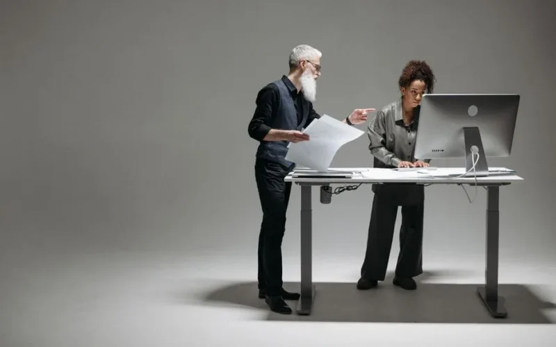 A senior man and a woman working together at a desk in a modern office setting, focusing on a project.