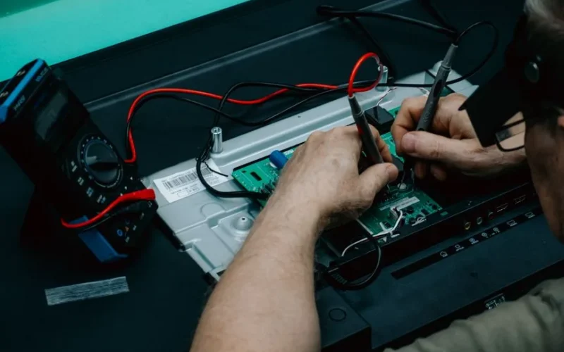 A technician uses a multimeter to repair a circuit board, focusing on precision electronics work.