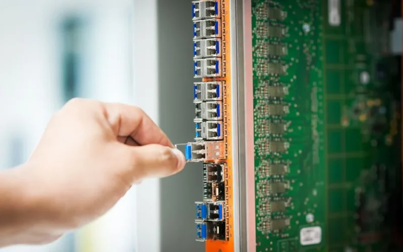 An individual connecting a cable into a network server port indoors, focusing on technology setup.